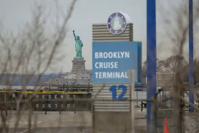 The Statute of Liberty looms in the background of a blue sign of the Brooklyn Cruise Terminal, which will temporarily house migrant men.